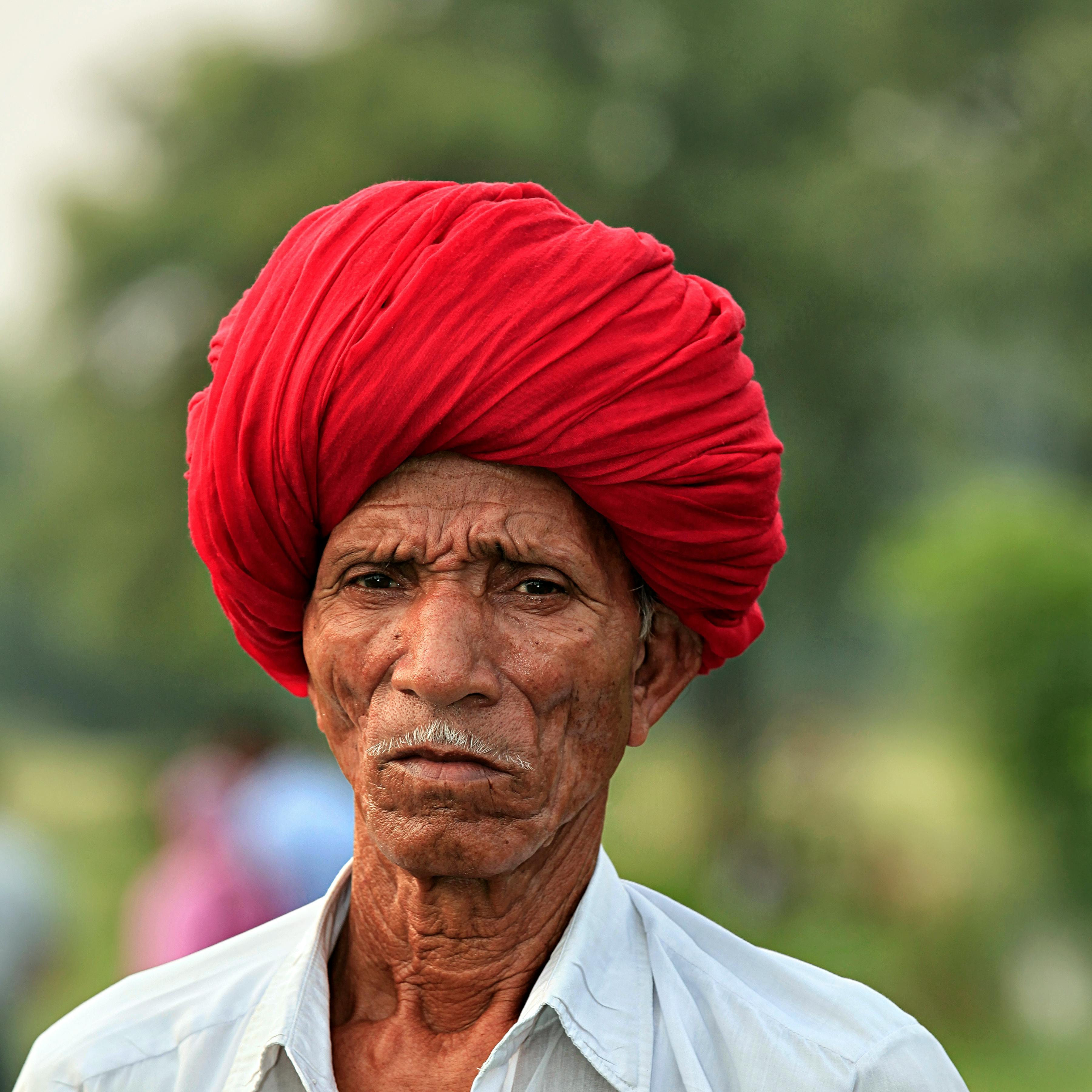 A vivid portrait of an elderly man with a red turban, captured outdoors.